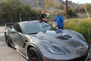 A gray Chevrolet Corvette Z06, front three quarters view with a Pacific Automotive independent repair shop technician shaking the hand of the driver. This represents Chevy repair and service San Diego.